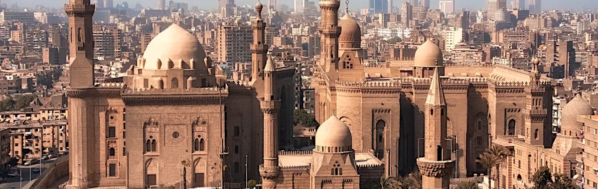 Aerial view of historic mosques with Cairo cityscape backdrop, showcasing Islamic architecture.