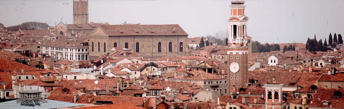 Panoramic aerial view of Venice showcasing red rooftops, towers, and historic architecture under a cloudy sky.