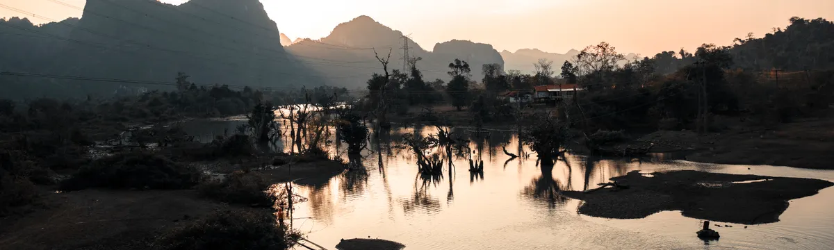 לאוס: Peaceful sunset view of a lake with mountain backdrop in Laos, reflecting serene beauty and nature's tranquility.