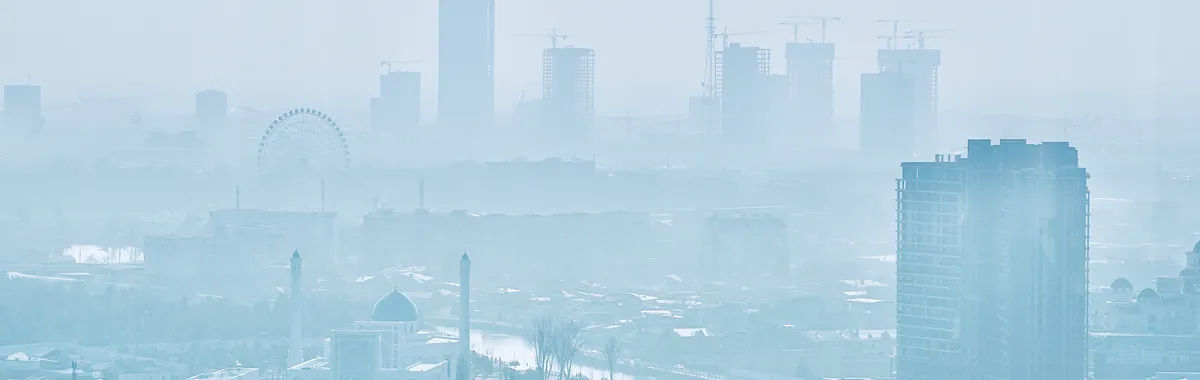 Aerial view of foggy Tashkent cityscape with buildings and ferris wheel.