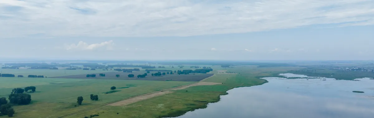 Drone shot of a vast lake and rural landscape in Kemerovo, Russia, showcasing serene nature.