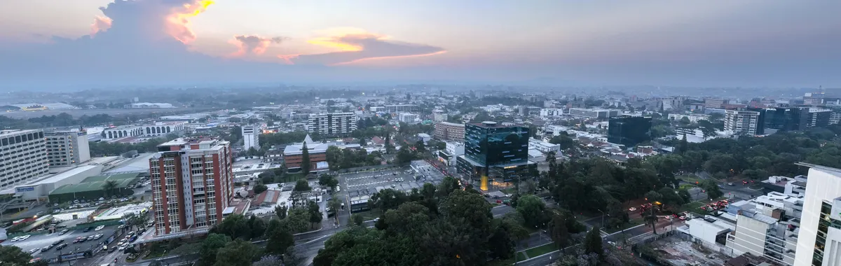 Panoramic aerial view of Guatemala City during sunset, showcasing urban landscape and skyline.