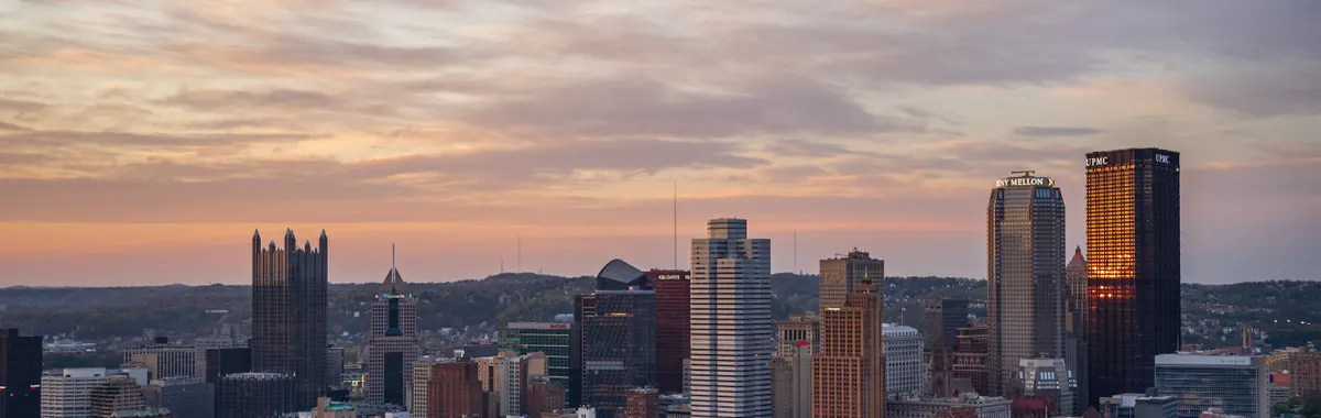 Stunning aerial view of Pittsburgh skyline with vibrant sunset colors in the sky.