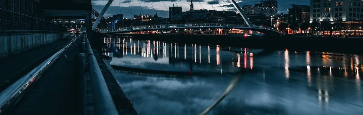 A stunning night view of Gateshead Millennium Bridge with city lights reflecting on the River Tyne.