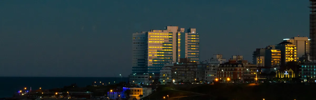 A vibrant skyline view of Mar del Plata, Argentina at twilight with city lights reflecting on the sea.