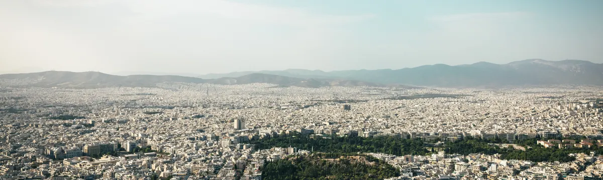יוון: Aerial view of Athens cityscape showcasing urban density with mountains in the background.