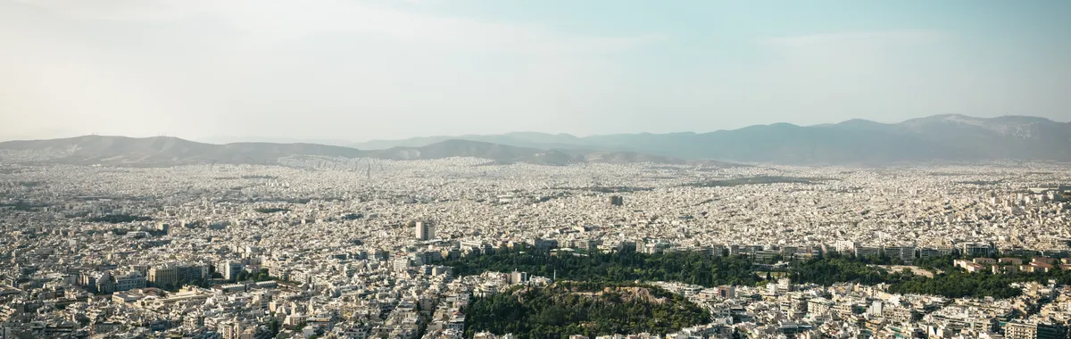 יוון: Aerial view of Athens cityscape showcasing urban density with mountains in the background.