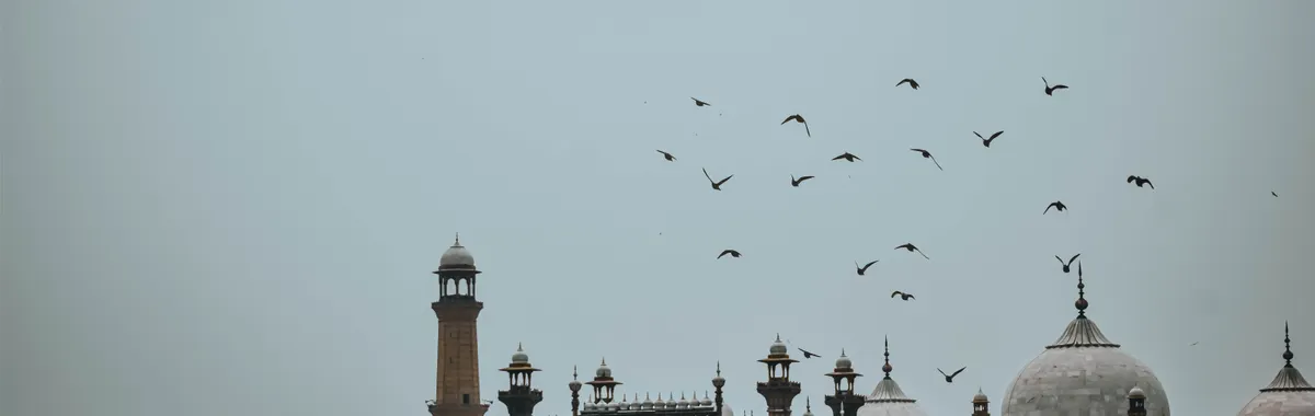 Scenic view of Badshahi Mosque in Lahore with flying birds against a clear blue sky.