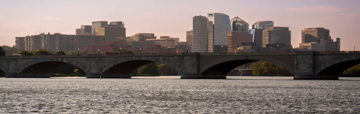 View of Arlington Memorial Bridge with modern skyline and calm river under twilight sky.
