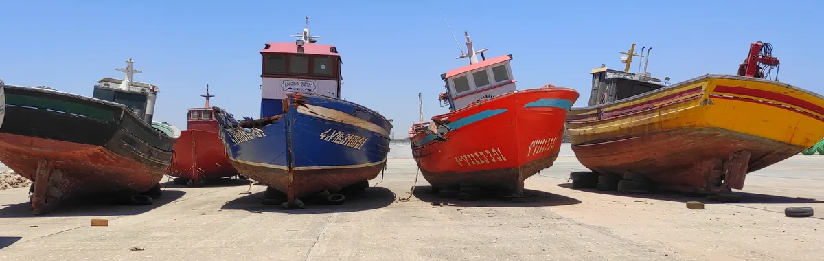 Fishing boats beached on a sunny day in Nouadhibou, Mauritania, showcasing vibrant colors under a clear sky.
