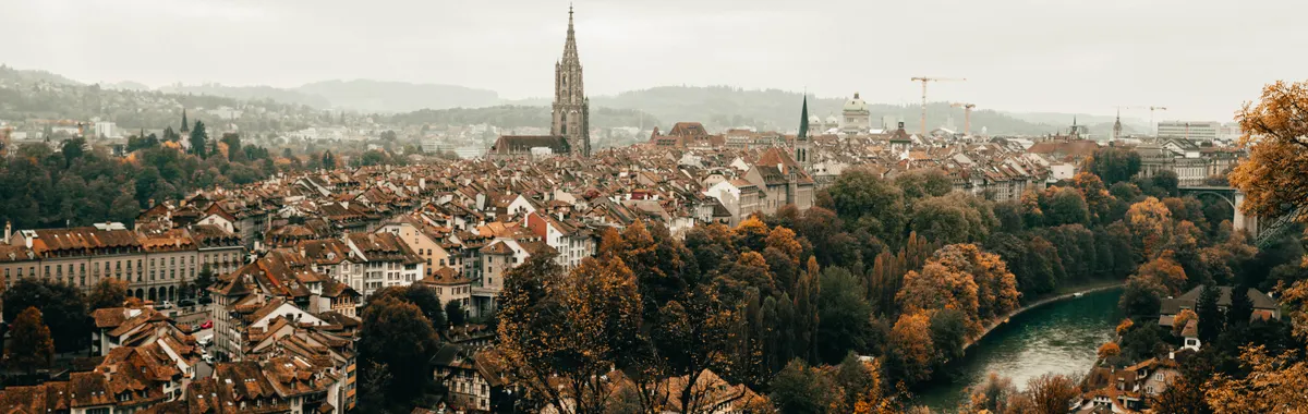 Scenic aerial photograph of Bern's historic old town during autumn, featuring the Cathedral of Bern and Aare River.