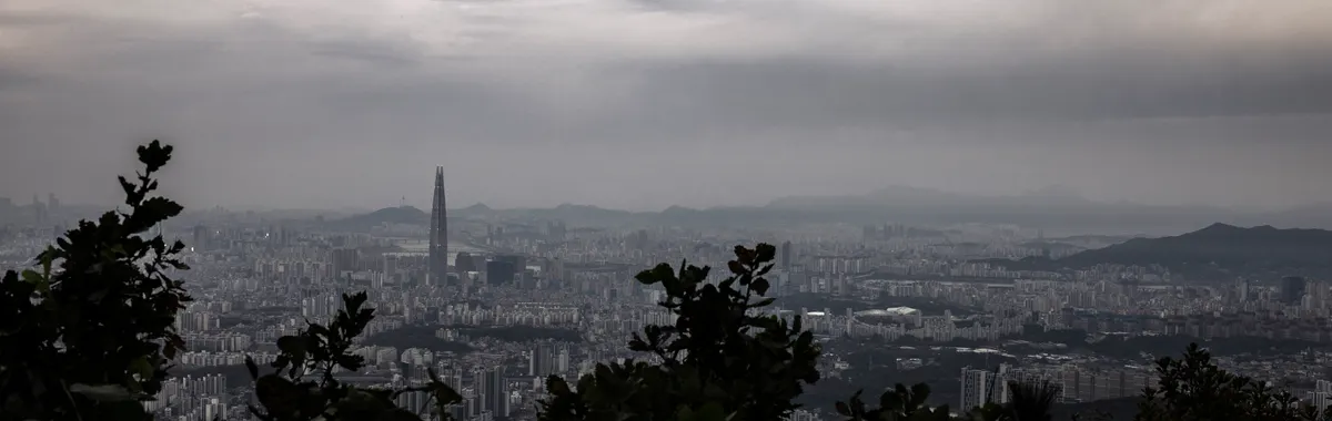 A dramatic aerial view of Gwangju cityscape with overcast skies and lush foreground.