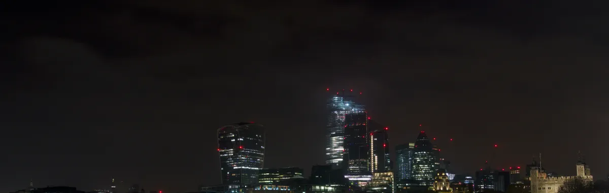Dramatic night view of London's skyline featuring modern skyscrapers and the historical Tower of London.