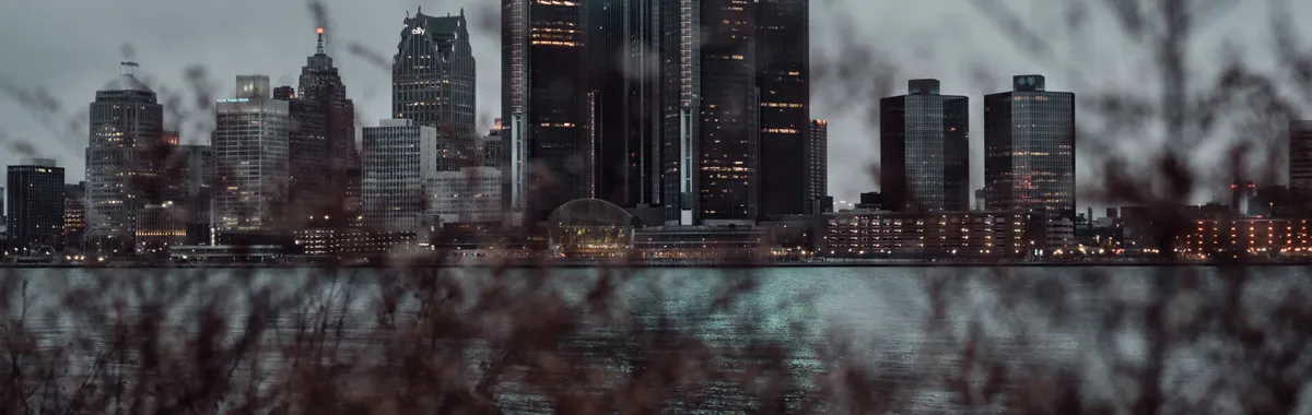 Dramatic view of the Detroit skyline across the waterfront at dusk, featuring skyscrapers.