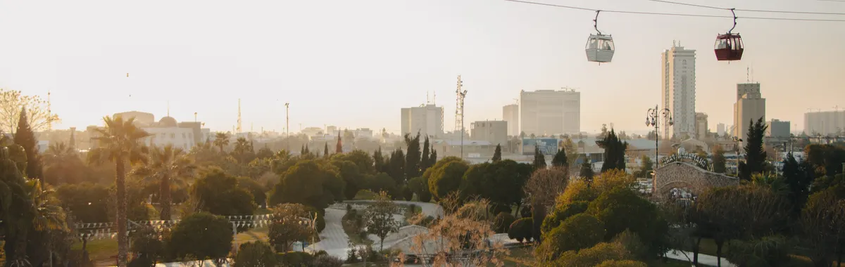 Stunning aerial view of a park in Erbil, Iraq with cable cars and the city skyline at sunset.