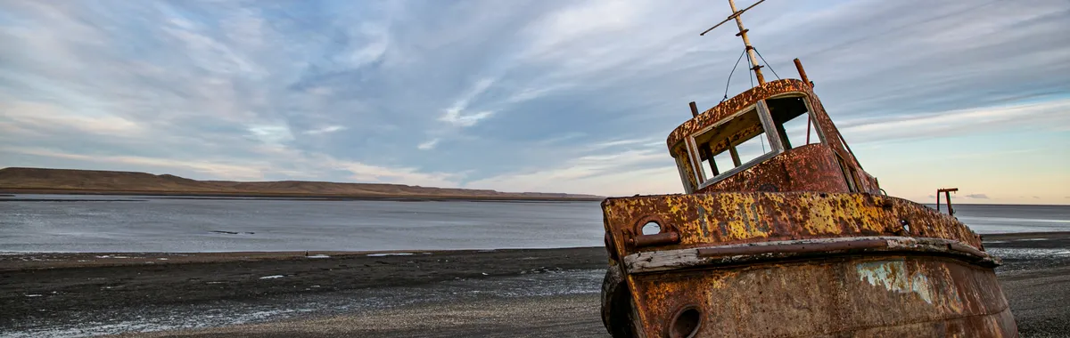 Abandoned rusty shipwreck on a pebbled beach at Río Gallegos, Santa Cruz, Argentina with dramatic sky.