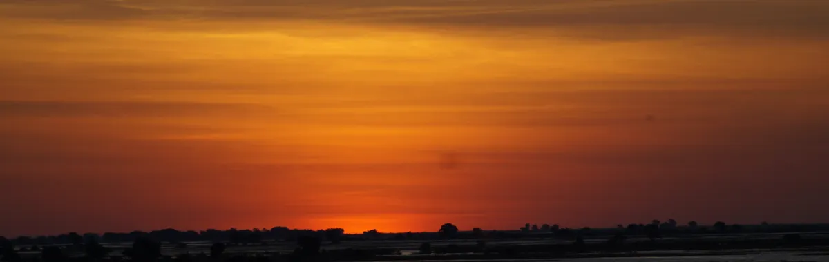 Stunning sunset over the wetlands in Maun, Botswana, highlighting a dramatic orange sky.