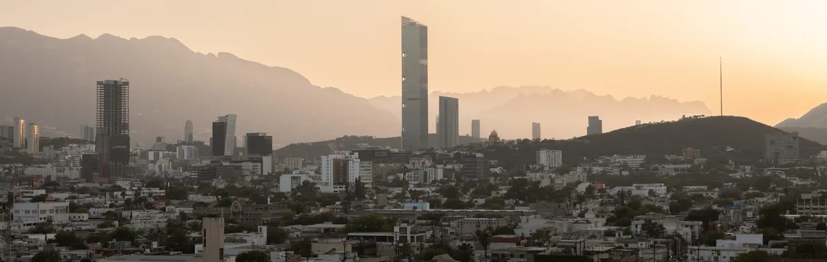 Aerial view of Monterrey's skyline at sunset, featuring modern skyscrapers and mountains.