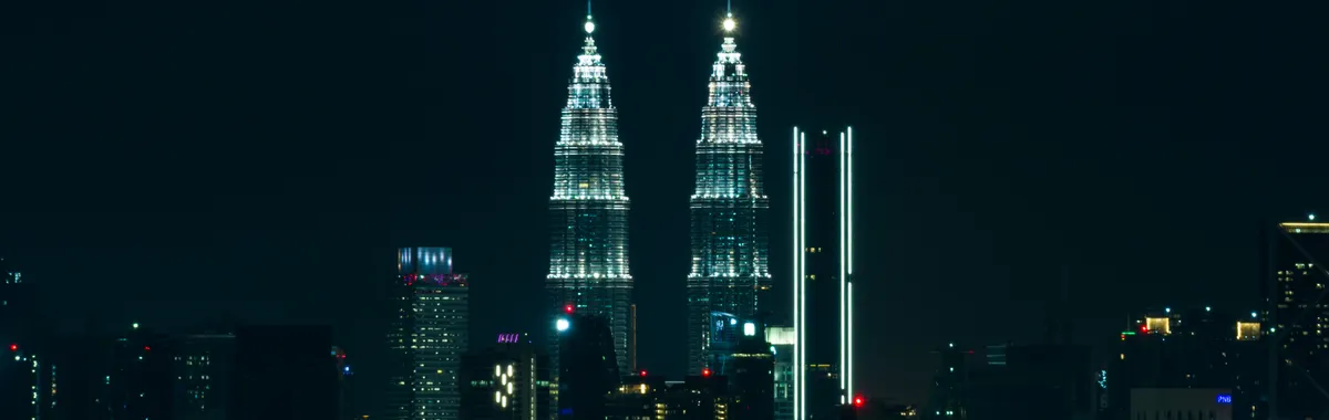 Breathtaking view of Kuala Lumpur's skyline at night featuring the iconic Petronas Towers illuminated against a dark sky.