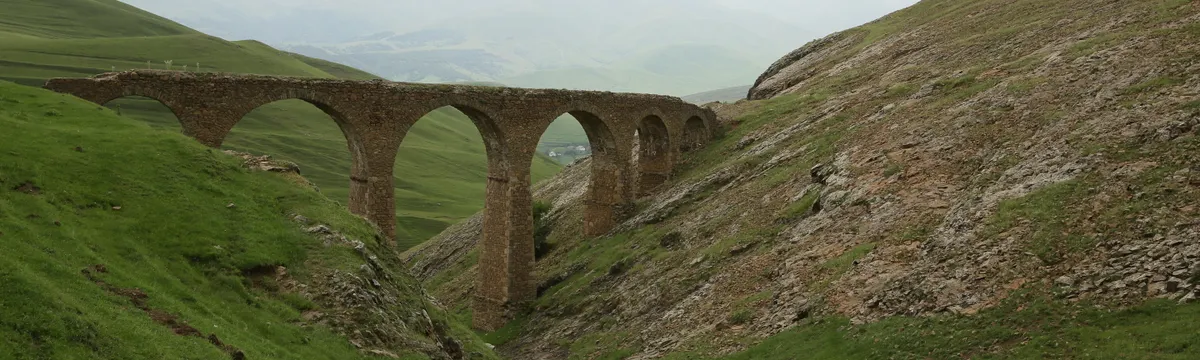 אזרבייג׳ן: A scenic view of a stone bridge arching over a lush green valley with distant hills.