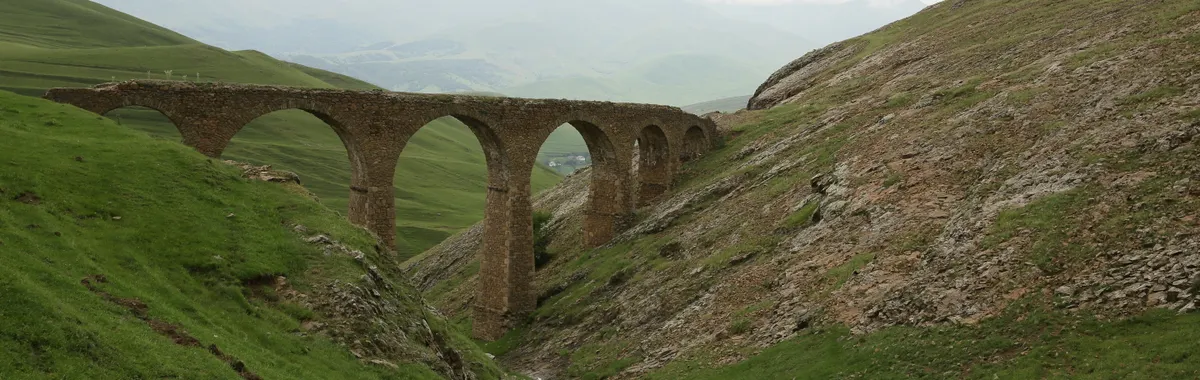 אזרבייג׳ן: A scenic view of a stone bridge arching over a lush green valley with distant hills.