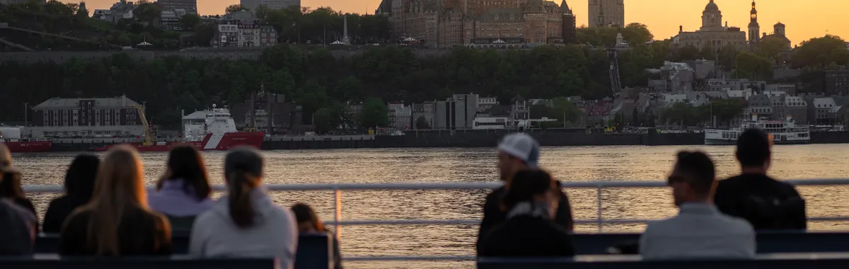 View of Château Frontenac and Quebec City skyline at sunset with people on a waterfront terrace.