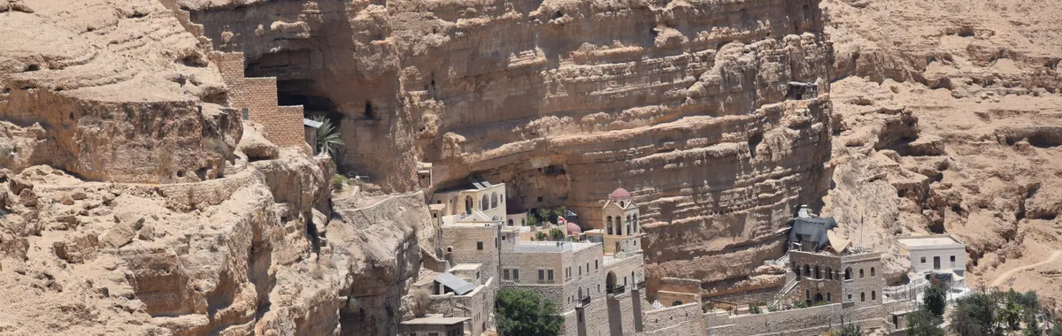 Aerial view of St George's Monastery nestled in the cliffs of Wadi Qelt, illuminated by bright sunlight.