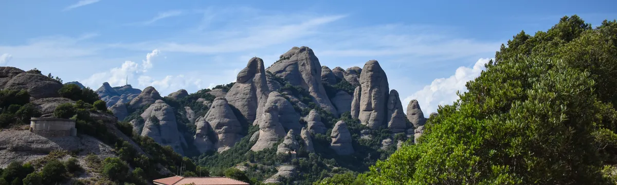 מונסראט: Stunning view of Montserrat mountains with lush greenery under clear blue skies in Spain.