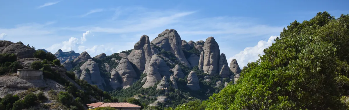 מונסראט: Stunning view of Montserrat mountains with lush greenery under clear blue skies in Spain.