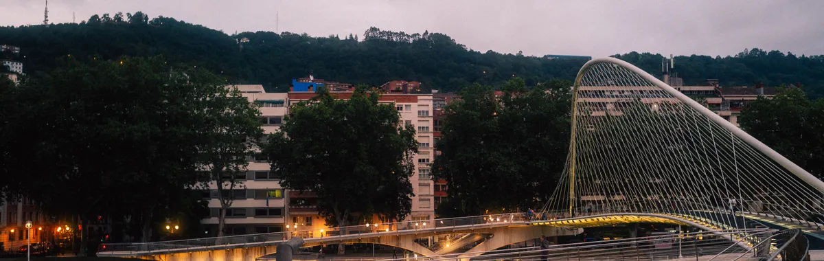 A modern architectural marvel, the Zubizuri Bridge in Bilbao lit up at dusk.