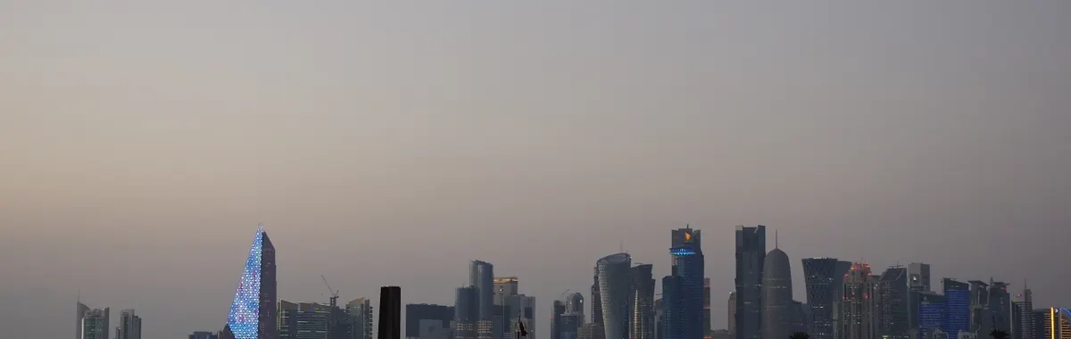 Scenic view of Doha city skyline with traditional dhow boat at dusk along the waterfront.