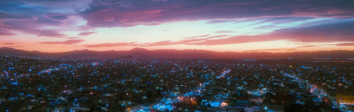 A stunning aerial view of Ciudad Nezahualcóyotl during sunset with vibrant city lights and colorful skies.
