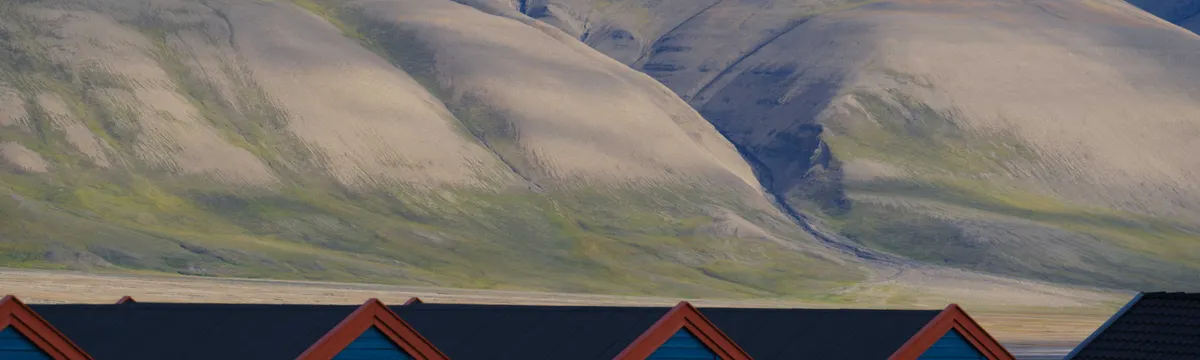 סבאלברד ויאן מאיין: Colorful cabins in Longyearbyen, Svalbard under Arctic mountains, showcasing polar beauty.