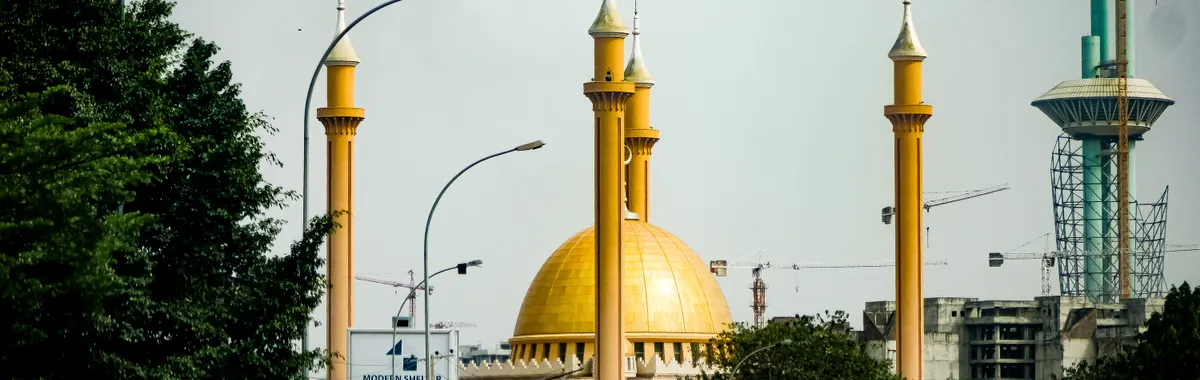 A bustling city street in Abuja featuring the iconic National Mosque and cars in traffic.