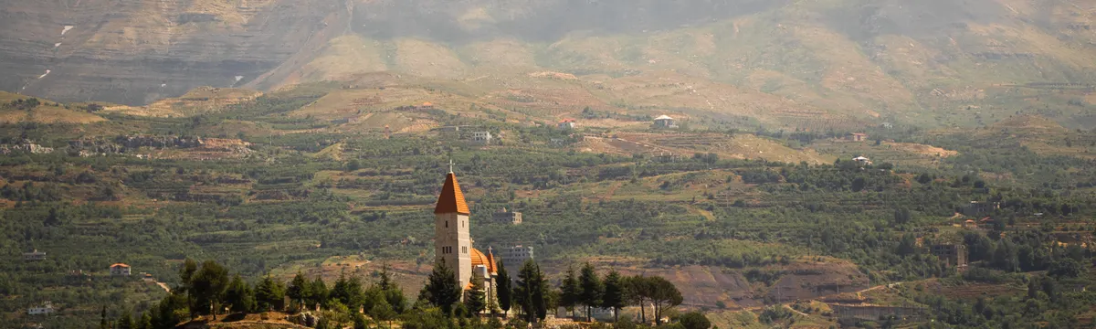 לבנון: Beautiful landscape of Bsharri, Lebanon, featuring a church amidst rolling hills and vibrant greenery.