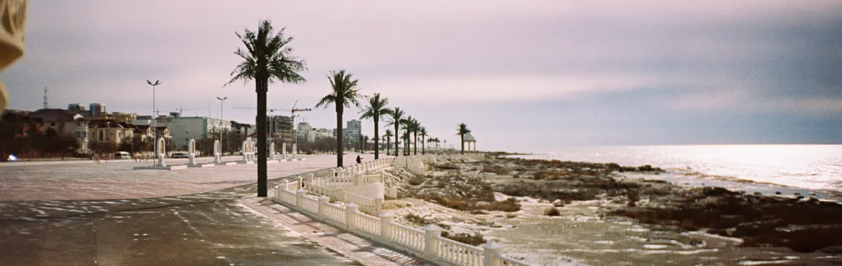 Scenic view of Aktau's coastline promenade with palm trees and serene sea.