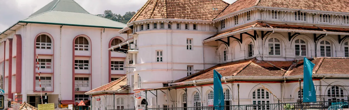 A vibrant street scene in Kandy, Sri Lanka featuring a historic building and a scooter rider.