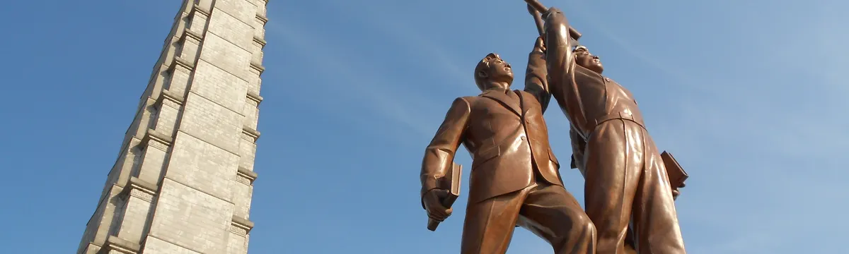 קוריאה הצפונית: Low angle view of Juche Tower and worker statues against a clear blue sky in Pyongyang, North Korea.