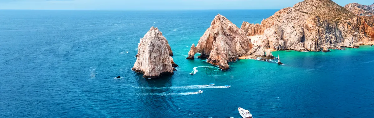 Stunning aerial shot of Cabo San Lucas Arch with vibrant blue ocean and boats in view.
