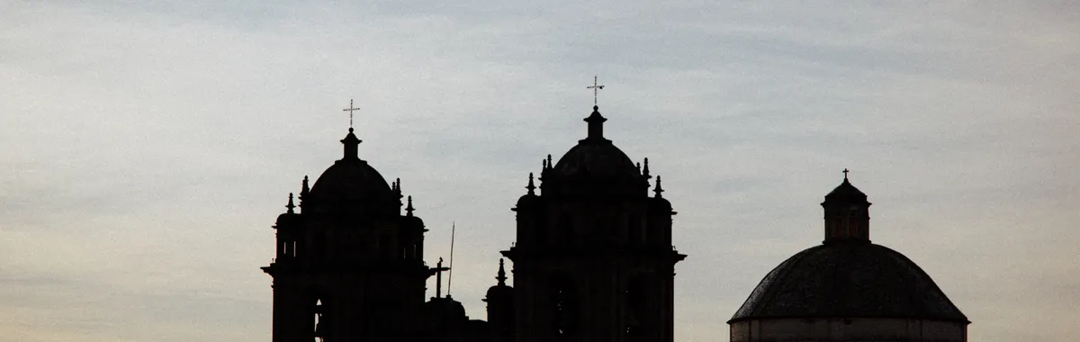 Silhouette of a historic church with domes and towers at dusk in Cusco, Peru.