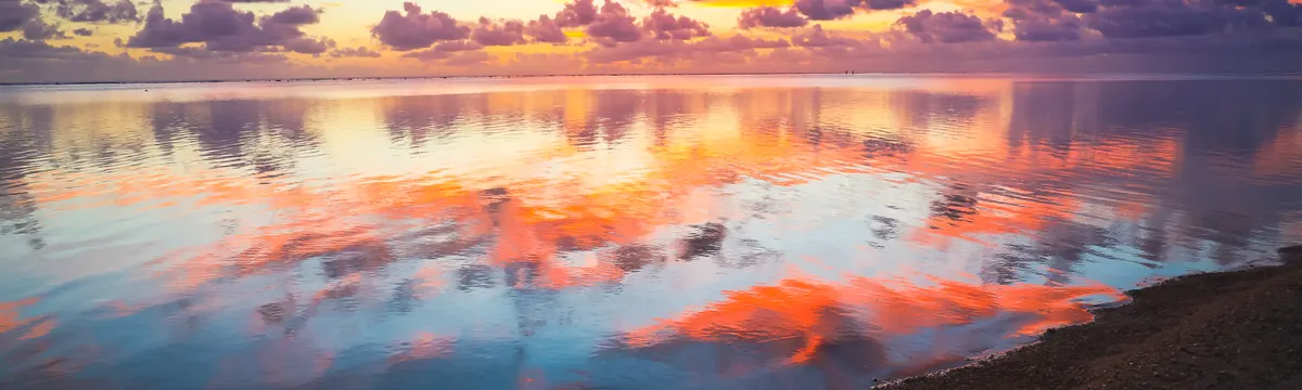 איי מריאנה הצפוניים: Breathtaking vibrant sunset over Saipan beach with mirror-like water reflections and colorful sky.