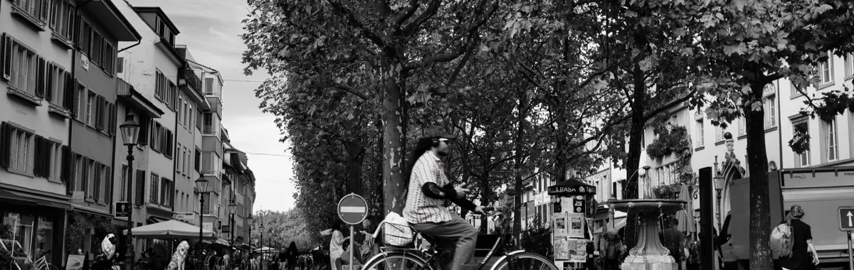 Black and white photo of a man cycling through a city street in Winterthur, Zurich, Switzerland, showcasing urban life.
