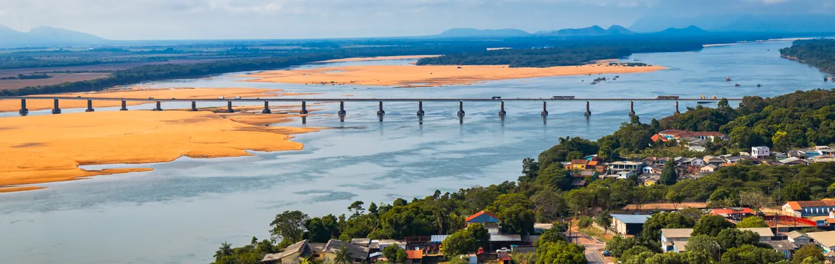 Scenic aerial view of a bridge crossing a river in Boa Vista, RR, with lush greenery and clear skies.