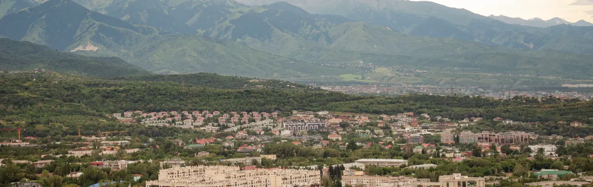A panoramic view of Almaty city with lush greenery and mountains in the background.