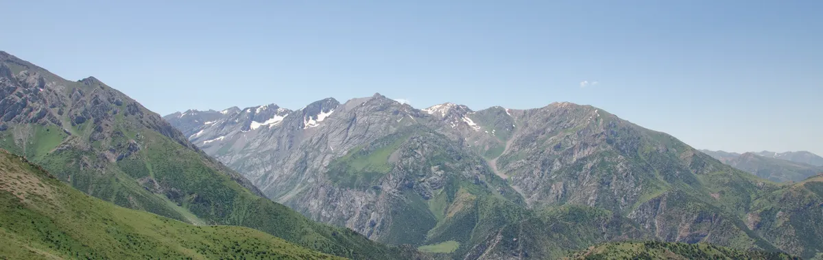 Stunning panoramic view of lush green mountains near Shymkent, Kazakhstan, under a clear blue sky.