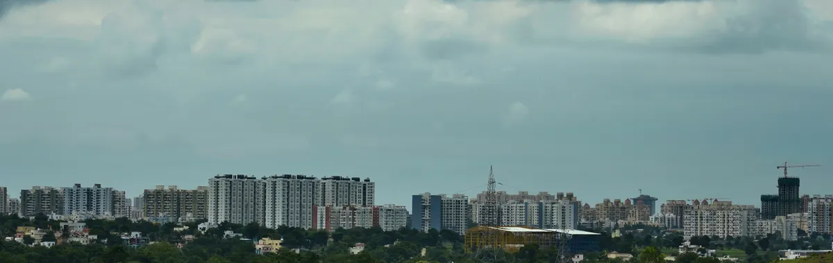 City skyline of Pune, Maharashtra with lush greenery and open gym equipment under dramatic cloudy skies.