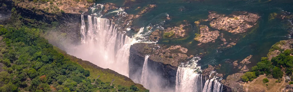 Breathtaking aerial view of Victoria Falls surrounded by lush greenery during summer day.