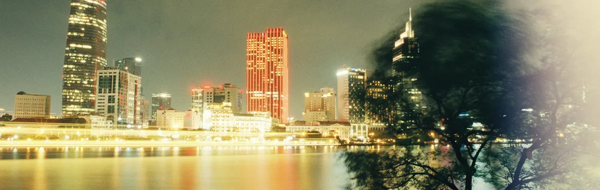 Stunning Ho Chi Minh City skyline with illuminated skyscrapers reflecting in the Saigon River at night.