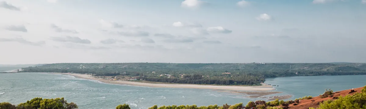 הודו: A picturesque view of Mandrem Beach with lush greenery and blue sky in Goa, India.