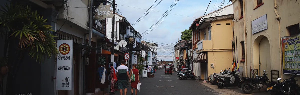 Historic street scene in Galle Fort, Sri Lanka with shops and pedestrians under a blue sky.